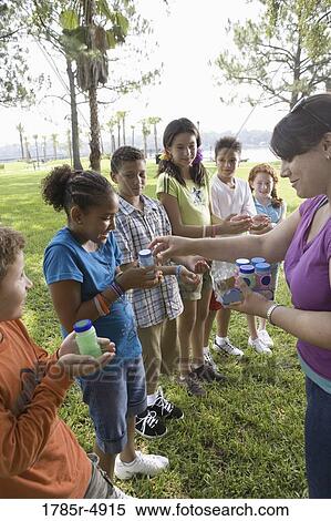 Teacher distributing bubble bottles to children at a park View Large Photo Image Stock Photography - Teacher distributing bubble bottles to children at a park. Fotosearch