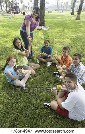 Teacher distributing cupcakes to children seated in a circle at a park View Large Photo Image Stock Photo - Teacher distributing cupcakes to children seated in a circle at a park. Fotosearch