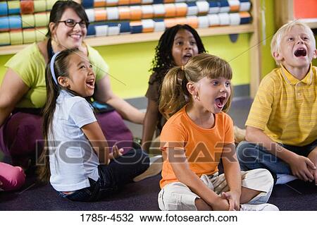 Teacher sitting and posing with students in a colorful classroom View Large Photo Image Stock Image - Teacher sitting and posing with students in a colorful classroom. Fotosearch