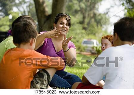 Teacher talking and gesturing to children while seated on the grass at a park View Large Photo Image Stock Image - Teacher talking and gesturing to children while seated on the grass at a park. Fotosearch