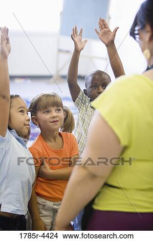 Picture - Teacher with her young students raising hands. Fotosearch