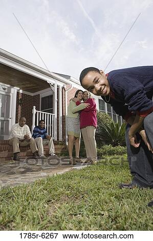 Teenager crouching and looking into camera with family in background View Large Photo Image Stock Photo - Teenager crouching and looking into camera with family in background. Fotosearch