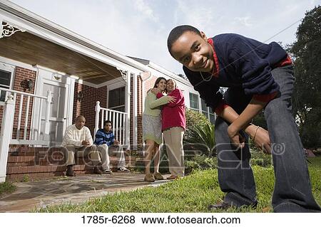 Teenager crouching and looking into camera with family in background View Large Photo Image Stock Photo - Teenager crouching and looking into camera with family in background. Fotosearch
