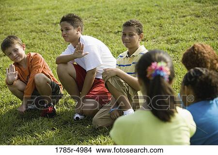 Picture - Three boys sitting on grass at a park, facing three girls. Fotosearch