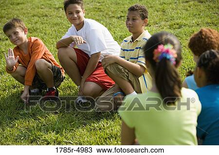 Three boys sitting on grass at a park, facing three girls View Large Photo Image Stock Image - Three boys sitting on grass at a park, facing three girls. Fotosearch
