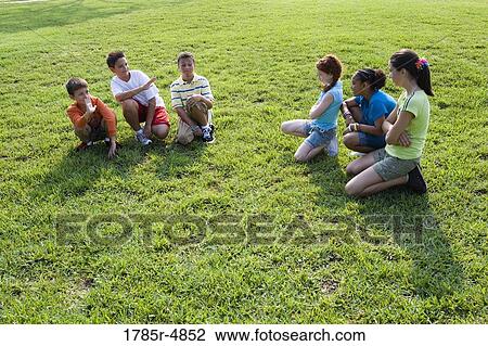 Three boys sitting opposite three girls on grass at a park View Large Photo Image Stock Image - Three boys sitting opposite three girls on grass at a park. Fotosearch