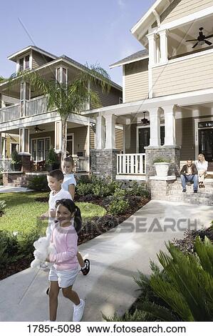 Stock Photo - Three children in front of their house while their parents watch from front steps. Fotosearch