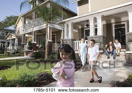 Stock Image - Three children play in front of their house while their parents watch from front steps. Fotosearch