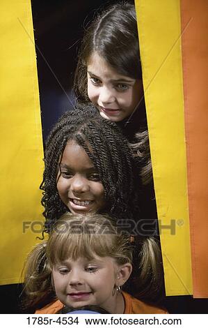 Picture - Three girls peeking out from behind a curtain. Fotosearch