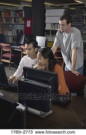 Stock Image - Three university students using computers in the library. Fotosearch