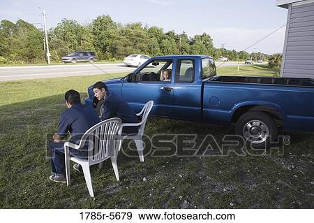 Two blue-collar men holding cold drinks sitting on lawn chairs next to parked old truck View Large Photo Image Stock Photo - Two blue-collar men holding cold drinks sitting on lawn chairs next to parked old truck. Fotosearch
