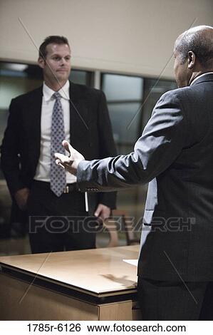 Stock Photograph - Two businessmen conversing in an office. Fotosearch