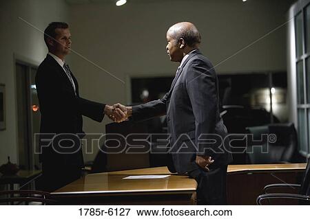 Stock Photo - Two businessmen shaking hands across an office desk. Fotosearch