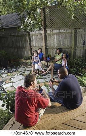Two families sitting together on backyard patio, enjoying cold drinks View Large Photo Image Stock Photo - Two families sitting together on backyard patio, enjoying cold drinks. Fotosearch