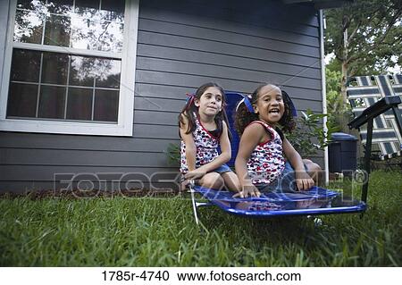 Two girls (6-7) sitting on lawn chair in backyard View Large Photo Image Stock Image - Two girls (6-7) sitting on lawn chair in backyard. Fotosearch