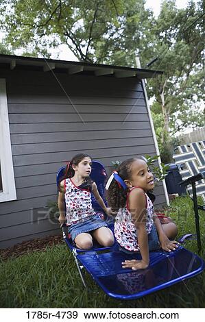 Two girls (6-7) sitting on lawn chair in backyard View Large Photo Image Stock Photo - Two girls (6-7) sitting on lawn chair in backyard. Fotosearch