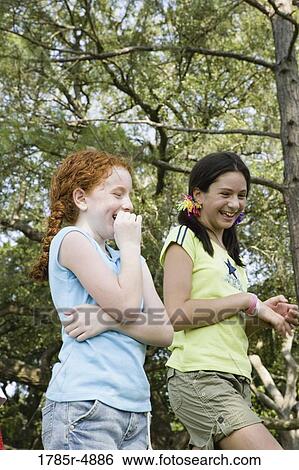 Two girls laughing together at a park View Large Photo Image Stock Photograph - Two girls laughing together at a park. Fotosearch