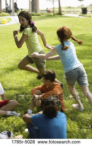 Stock Photo - Two girls running around children sitting in a circle on the grass. Fotosearch