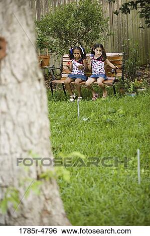 Two girls sitting on bench in the eating and drinking View Large Photo Image Stock Photograph - Two girls sitting on bench in the eating and drinking. Fotosearch