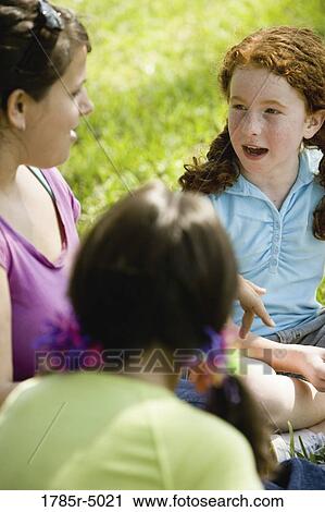 Two girls talking to their teacher while sitting on the grass View Large Photo Image Stock Image - Two girls talking to their teacher while sitting on the grass. Fotosearch