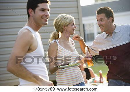 Two men and a woman enjoying a cookout in front of a trailer home View Large Photo Image Stock Photo - Two men and a woman enjoying a cookout in front of a trailer home. Fotosearch