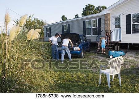 Stock Photo - Two men looking under the hood of a pickup truck in front of trailer home. Fotosearch