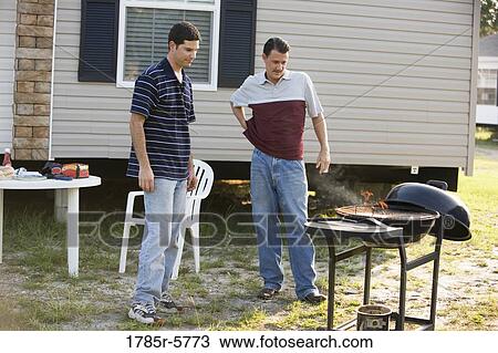Stock Image - Two men preparing a cookout in front of trailer home. Fotosearch