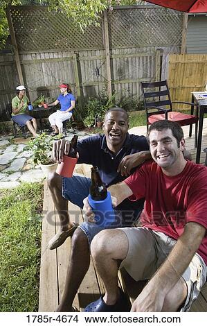 Two men sitting on steps of backyard patio, toasting with their cold beverages, two women sitting in background View Large Photo Image Picture - Two men sitting on steps of backyard patio, toasting with their cold beverages, two women sitting in background. Fotosearch