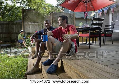 Two men sitting on steps of backyard patio, two women sitting in background View Large Photo Image Stock Image - Two men sitting on steps of backyard patio, two women sitting in background. Fotosearch
