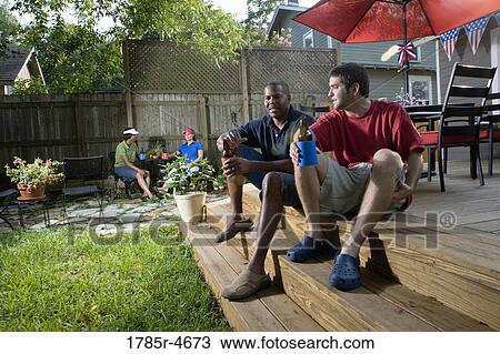 Two men sitting on steps of backyard patio, two women sitting in background View Large Photo Image Stock Image - Two men sitting on steps of backyard patio, two women sitting in background. Fotosearch