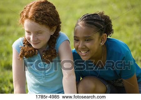 Stock Photography - Two mischievous girls sitting together on the grass. Fotosearch