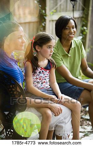 Two women and a young girl sitting in backyard View Large Photo Image Stock Image - Two women and a young girl sitting in backyard. Fotosearch
