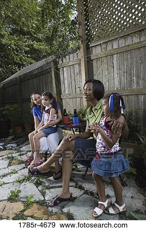 Two women sitting together on backyard patio with their young daughters View Large Photo Image Stock Photo - Two women sitting together on backyard patio with their young daughters. Fotosearch