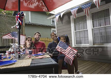 Two young girls with dads at 4th of July cookout waving American flags View Large Photo Image Picture - Two young girls with dads at 4th of July cookout waving American flags. Fotosearch