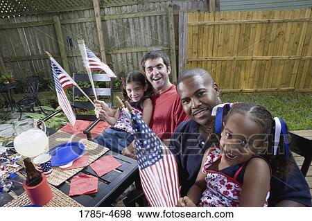 Two young girls with dads at 4th of July cookout waving American flags View Large Photo Image Stock Photo - Two young girls with dads at 4th of July cookout waving American flags. Fotosearch