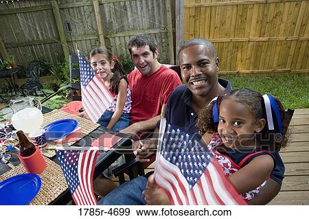 Stock Photo - Two young girls with dads at 4th of July cookout waving American flags. Fotosearch