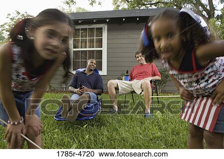 Two young men sitting on lawn chairs enjoying a beer while daughters play View Large Photo Image Stock Image - Two young men sitting on lawn chairs enjoying a beer while daughters play. Fotosearch