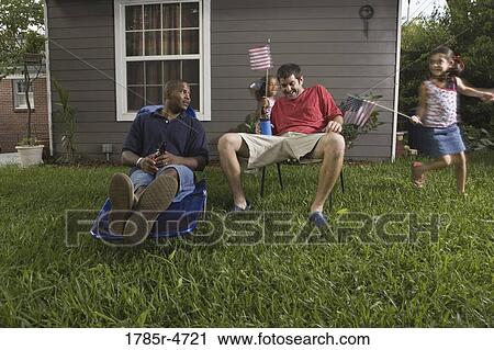 Two young men sitting on lawn chairs enjoying a beer while daughters play View Large Photo Image Stock Image - Two young men sitting on lawn chairs enjoying a beer while daughters play. Fotosearch