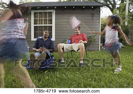 Two young men sitting on lawn chairs enjoying a beer while daughters play View Large Photo Image Stock Photo - Two young men sitting on lawn chairs enjoying a beer while daughters play. Fotosearch