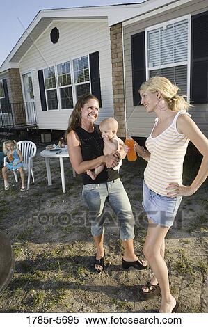 Stock Photography - Two young women conversing in backyard with children. Fotosearch