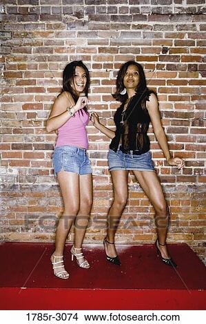 Two young women in hip-hop fashion standing suggestively against brick wall View Large Photo Image Picture - Two young women in hip-hop fashion standing suggestively against brick wall. Fotosearch