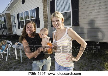 Stock Photo - Two young women with baby standing outside trailer home. Fotosearch
