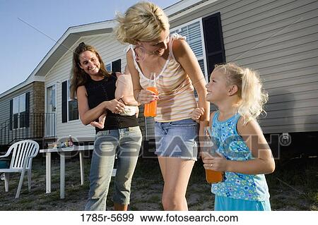 Stock Photo - Two young women with children standing outside trailer home. Fotosearch