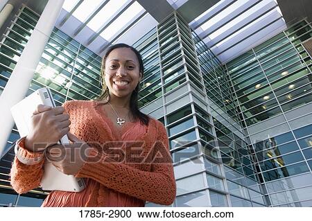 Stock Image - University student standing outside campus building. Fotosearch