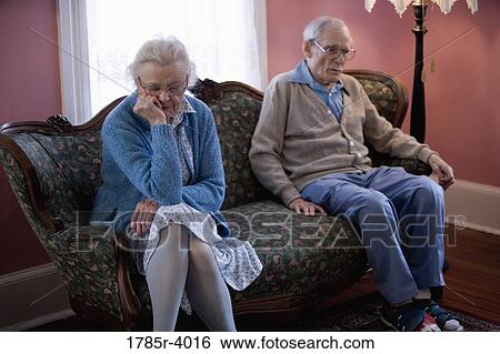 Upset elderly couple sitting on sofa View Large Photo Image Stock Photograph - Upset elderly couple sitting on sofa. Fotosearch