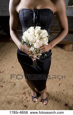 Stock Photo - View below the shoulders of a woman in black holding a bouquet of white roses. Fotosearch