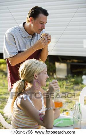 View of a happy couple eating and drinking at a cookout in front of a trailer home View Large Photo Image Stock Photograph - View of a happy couple eating and drinking at a cookout in front of a trailer home. Fotosearch