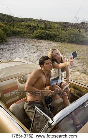 View of a young couple in antique convertible car looking at photographs View Large Photo Image Stock Image - View of a young couple in antique convertible car looking at photographs. Fotosearch