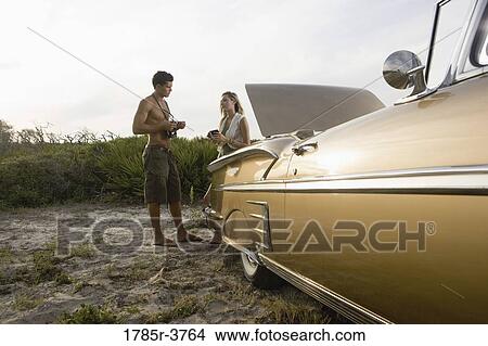 View of a young couple standing by antique convertible car View Large Photo Image Picture - View of a young couple standing by antique convertible car. Fotosearch