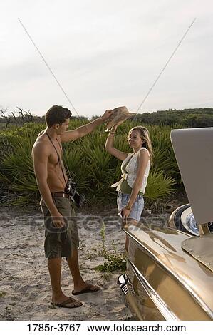 Stock Photo - View of a young couple standing by antique convertible car. Fotosearch